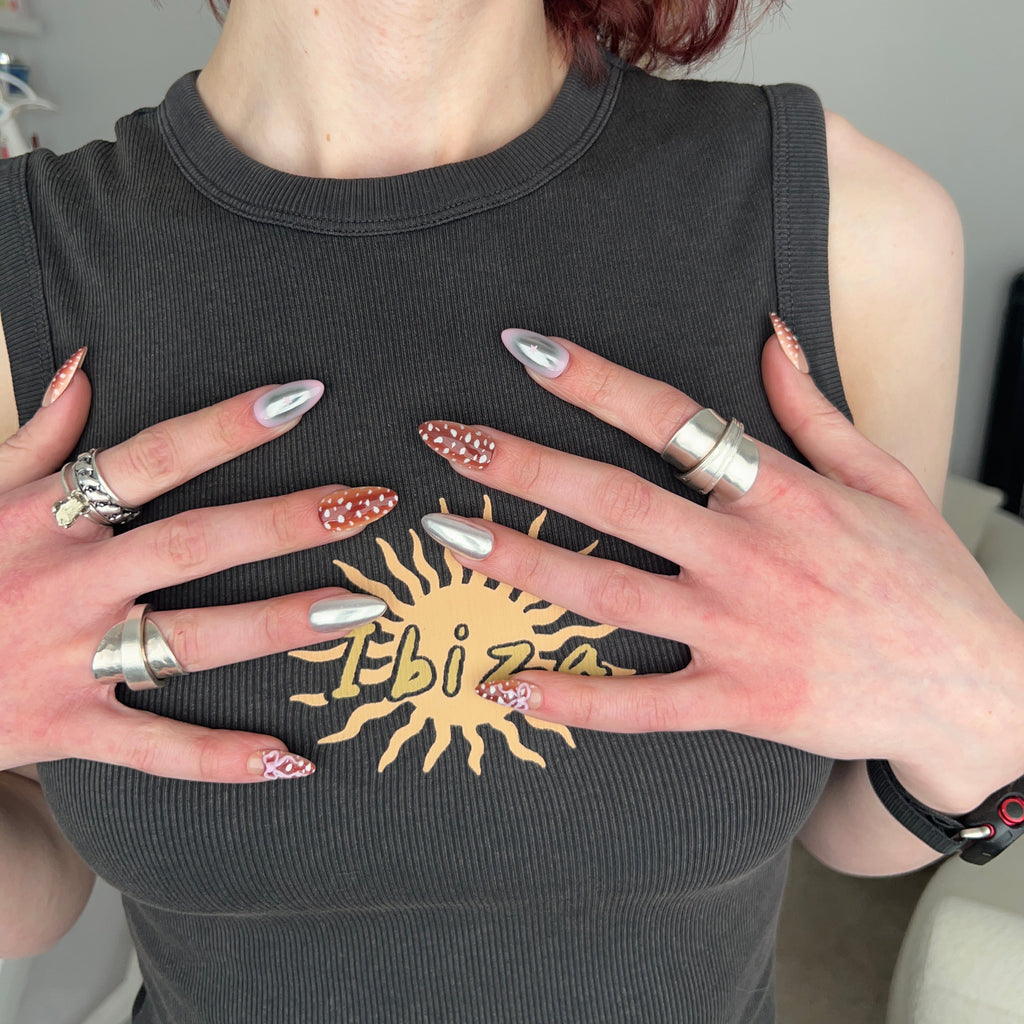 Person wearing a black tank top with a gold sun design, holding their hands up to show off nail polish and rings.