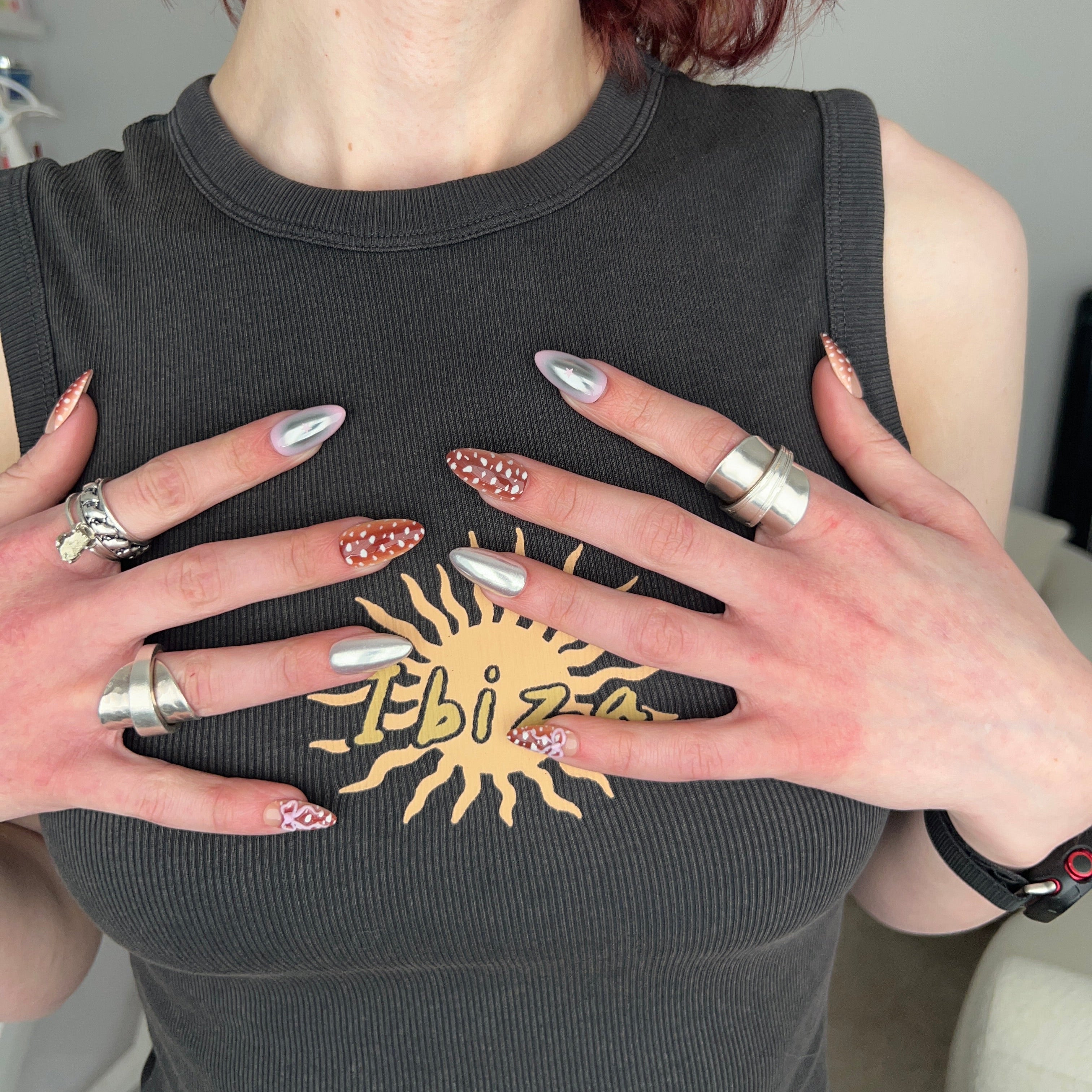 Person wearing a black tank top with a gold sun design, holding their hands up to show off nail polish and rings.